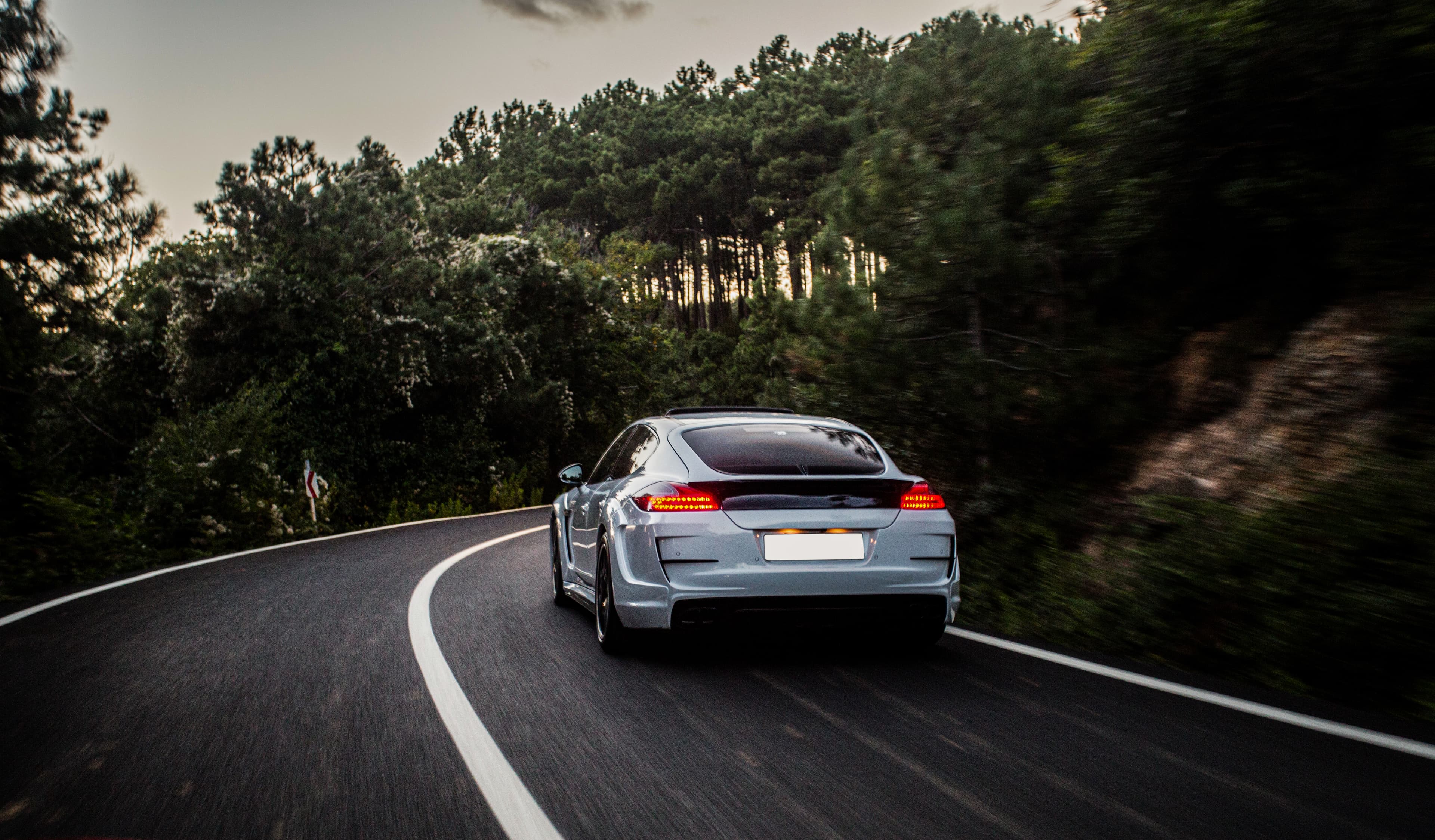 Silver car driving along a winding road through a forest